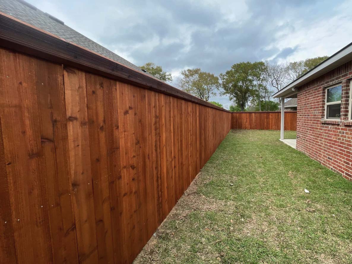 Full privacy wood fence with beveled edge top cap trim installed around a yard