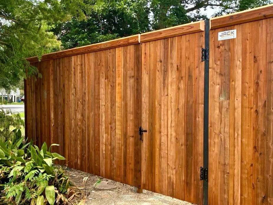 Full privacy wood fence and gate with beveled edge top cap trim installed around a yard
